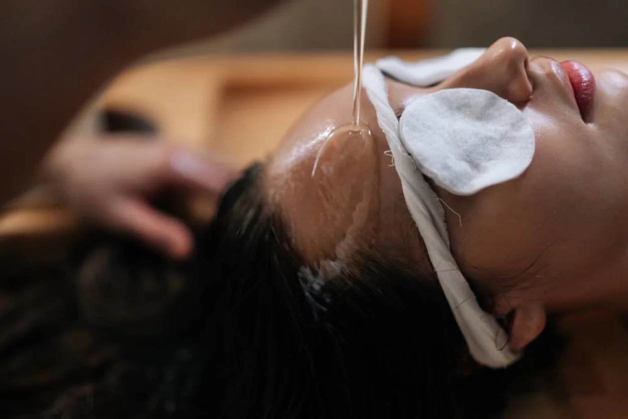 Close up face of woman with cotton pads over eyes while receiving Shirodhara oil treatment